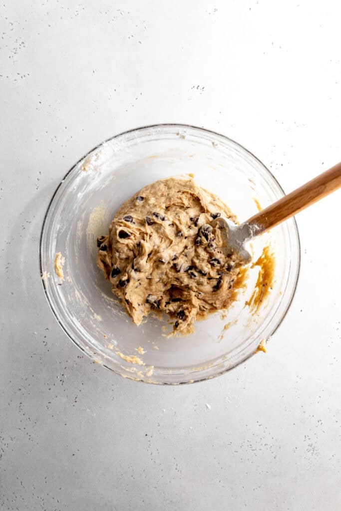 Banana chocolate chip cookie dough in a glass bowl with a rubber spatula.