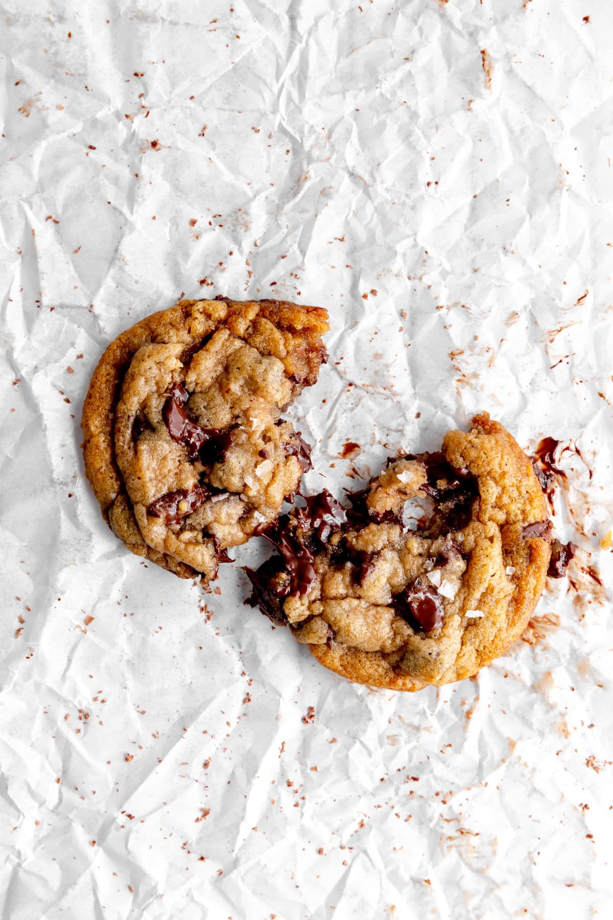 Banana chocolate chip cookie broken in half on white parchment paper.