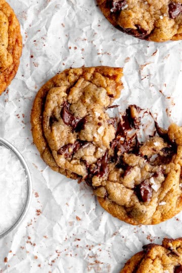 Banana chocolate chip cookie broken in half and a cup of flaky salt.