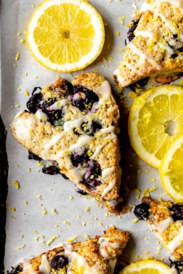 Lemon blueberry scones on a baking sheet with lemon slices and a linen napkin.