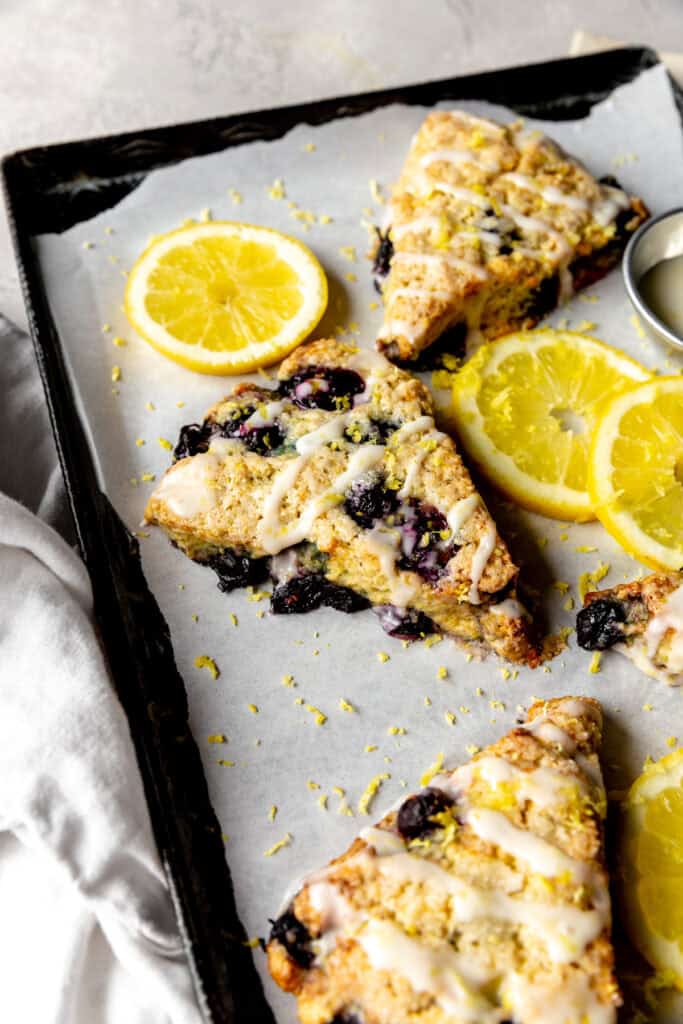 Lemon blueberry scone on a baking sheet with lemon slices.