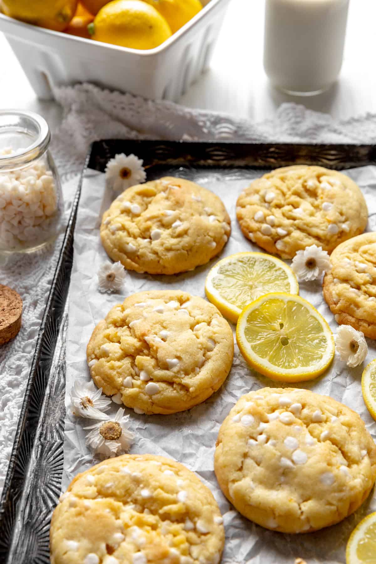 Lemon white chocolate cookies, a jar of white chocolate chips and a basket of lemons.