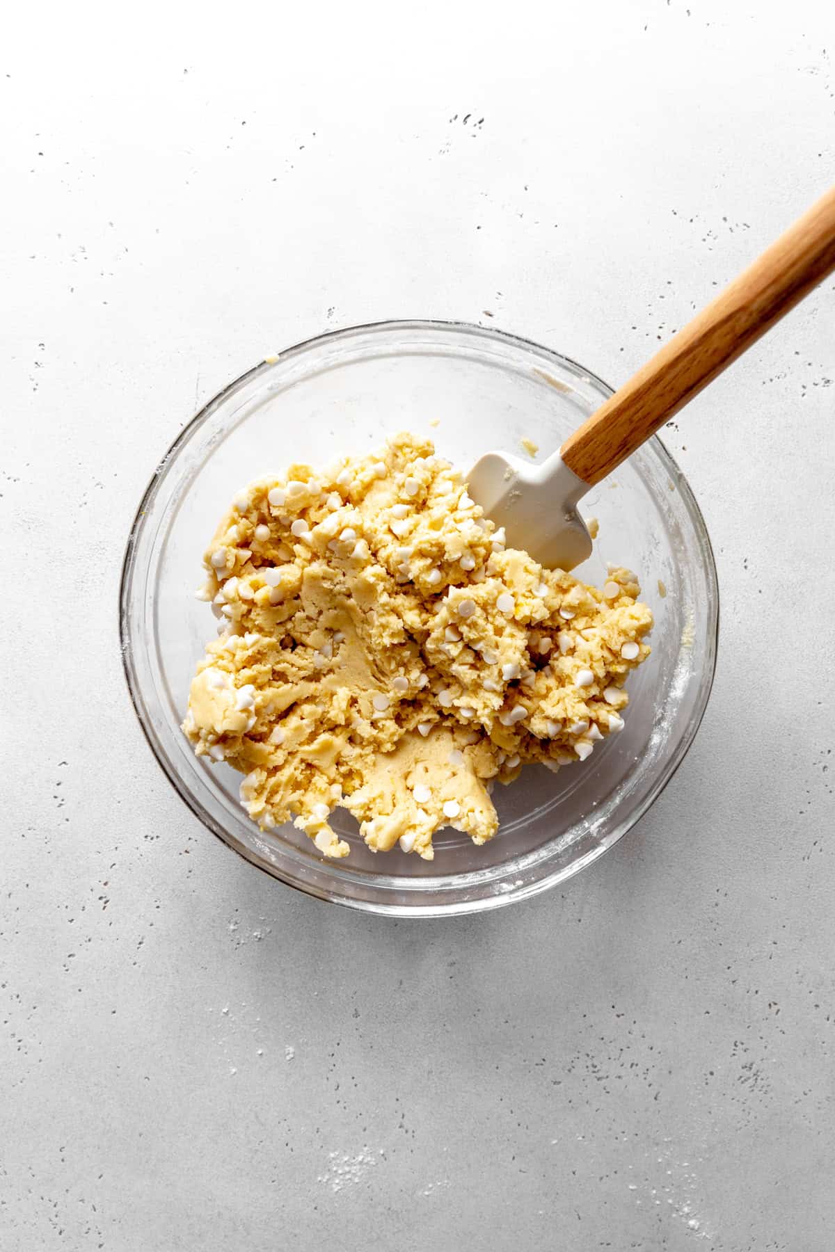 Lemon white chocolate cookies dough in a glass bowl with a rubber spatula.