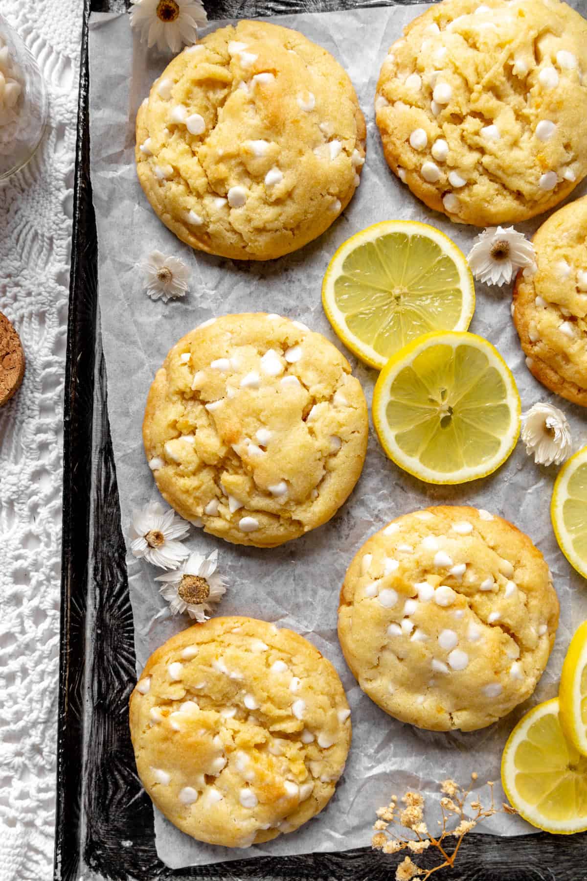Lemon white chocolate cookies and fresh lemon slices on a baking sheet.