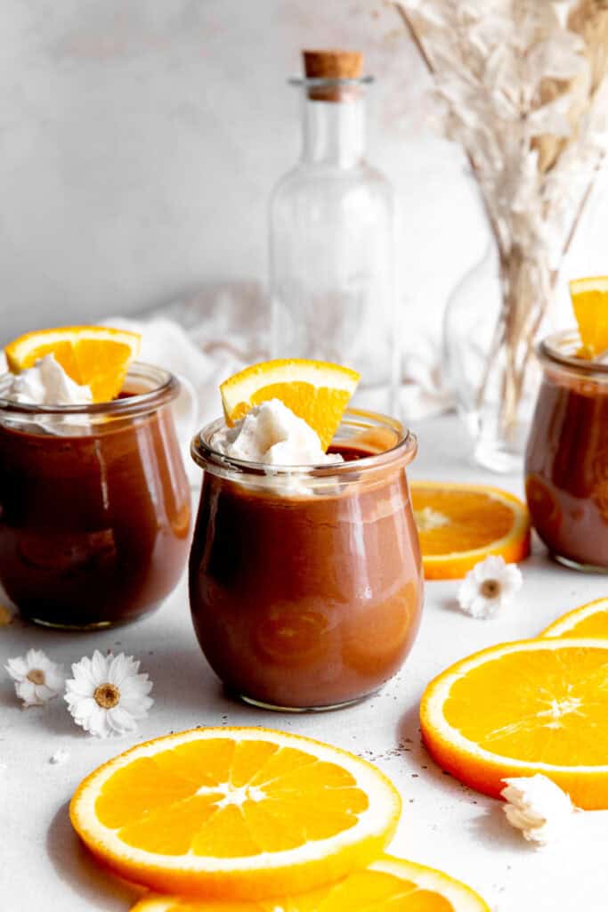 Glass jars of chocolate mousse topped with whipped cream and orange.