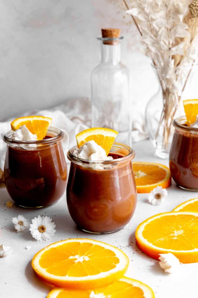 Glass jars of chocolate mousse, a white linen napkin and orange slices.