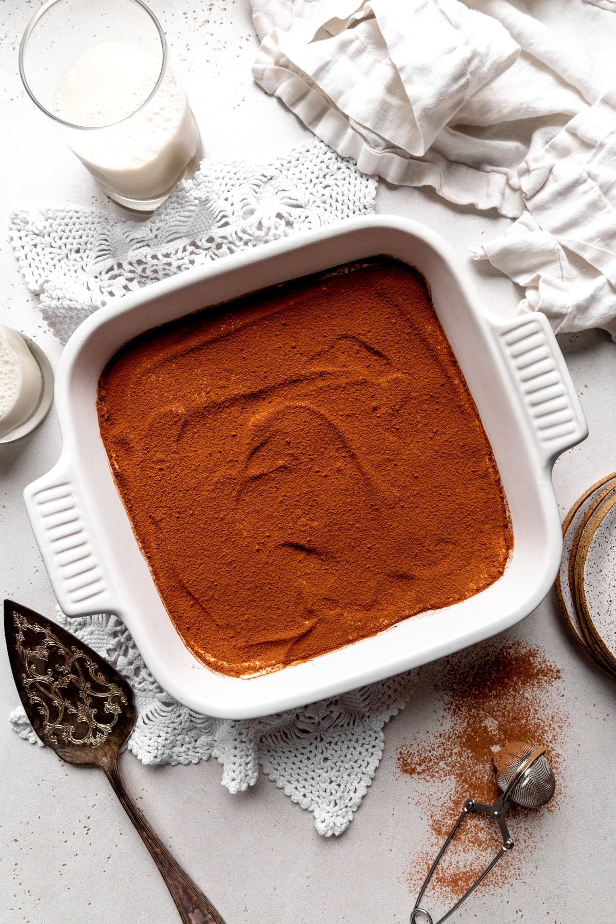 Tiramisu in a square dish, a glass of milk and a linen napkin.