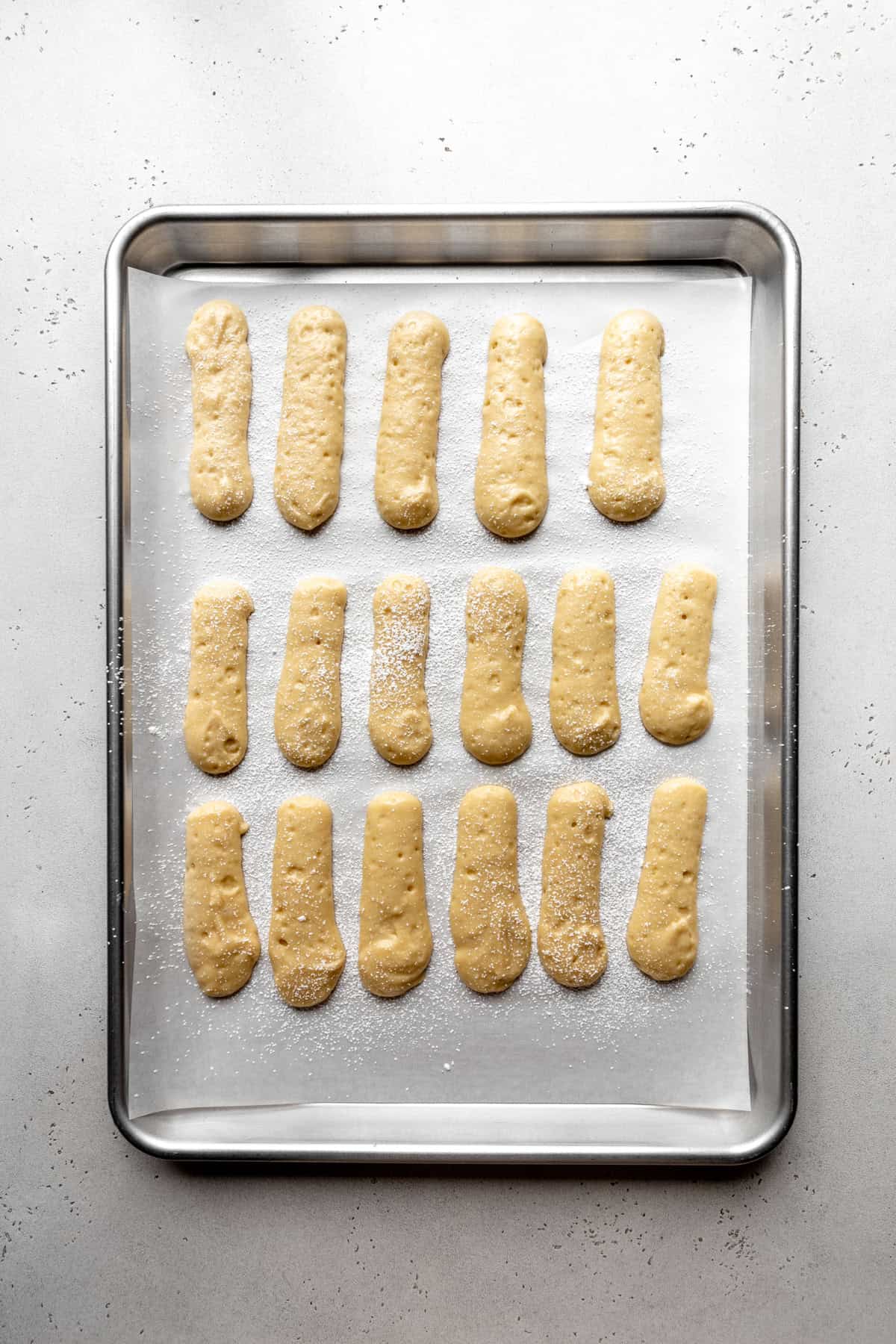 Unbaked ladyfingers on a baking sheet.