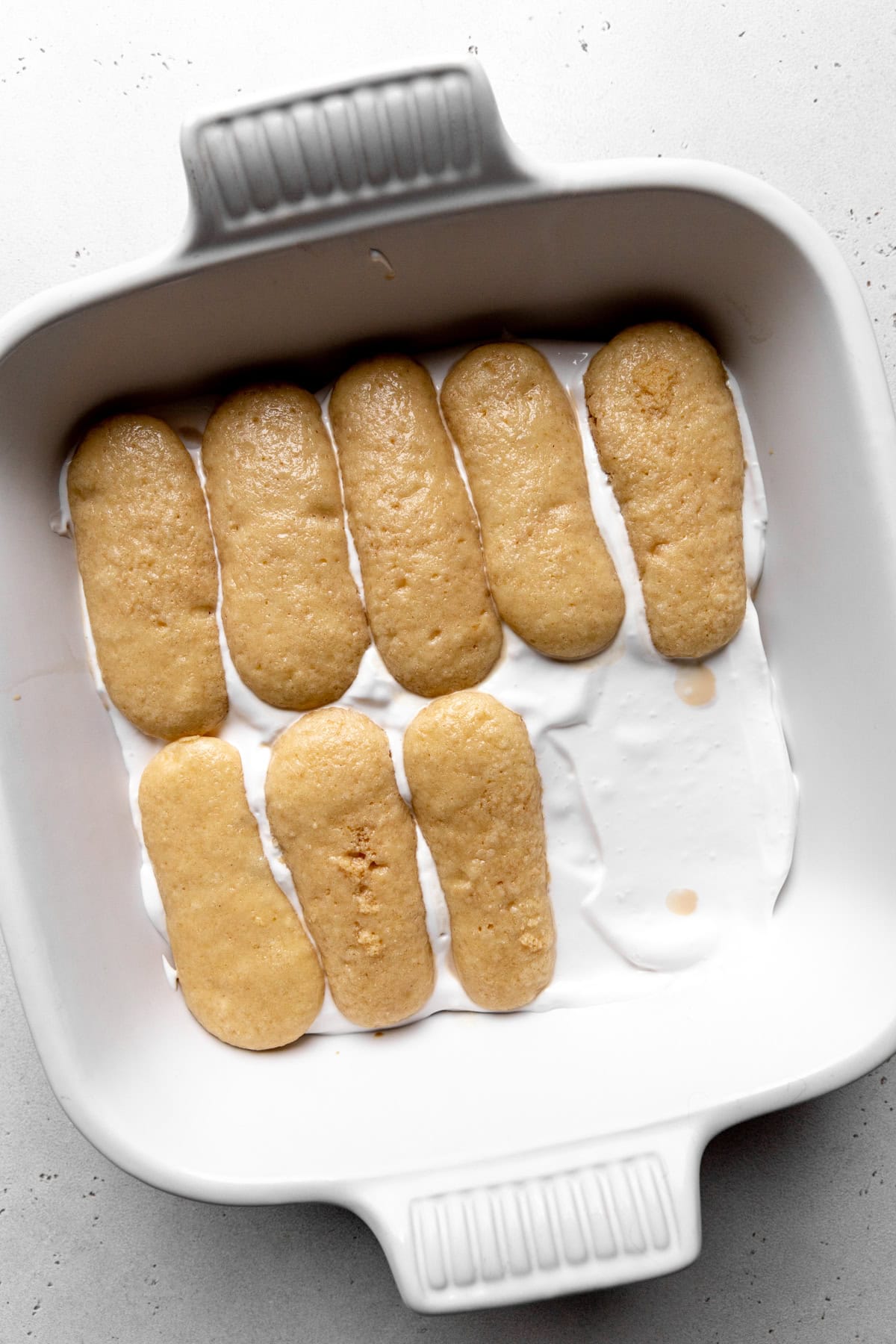 Ladyfingers layered with mascarpone in a square dish.