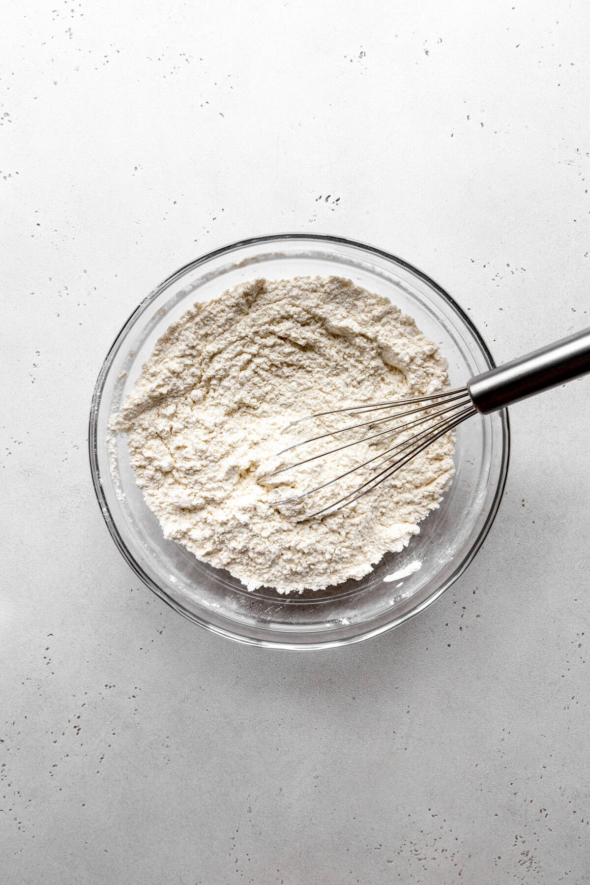 Glass bowl of flour and a wire whisk.