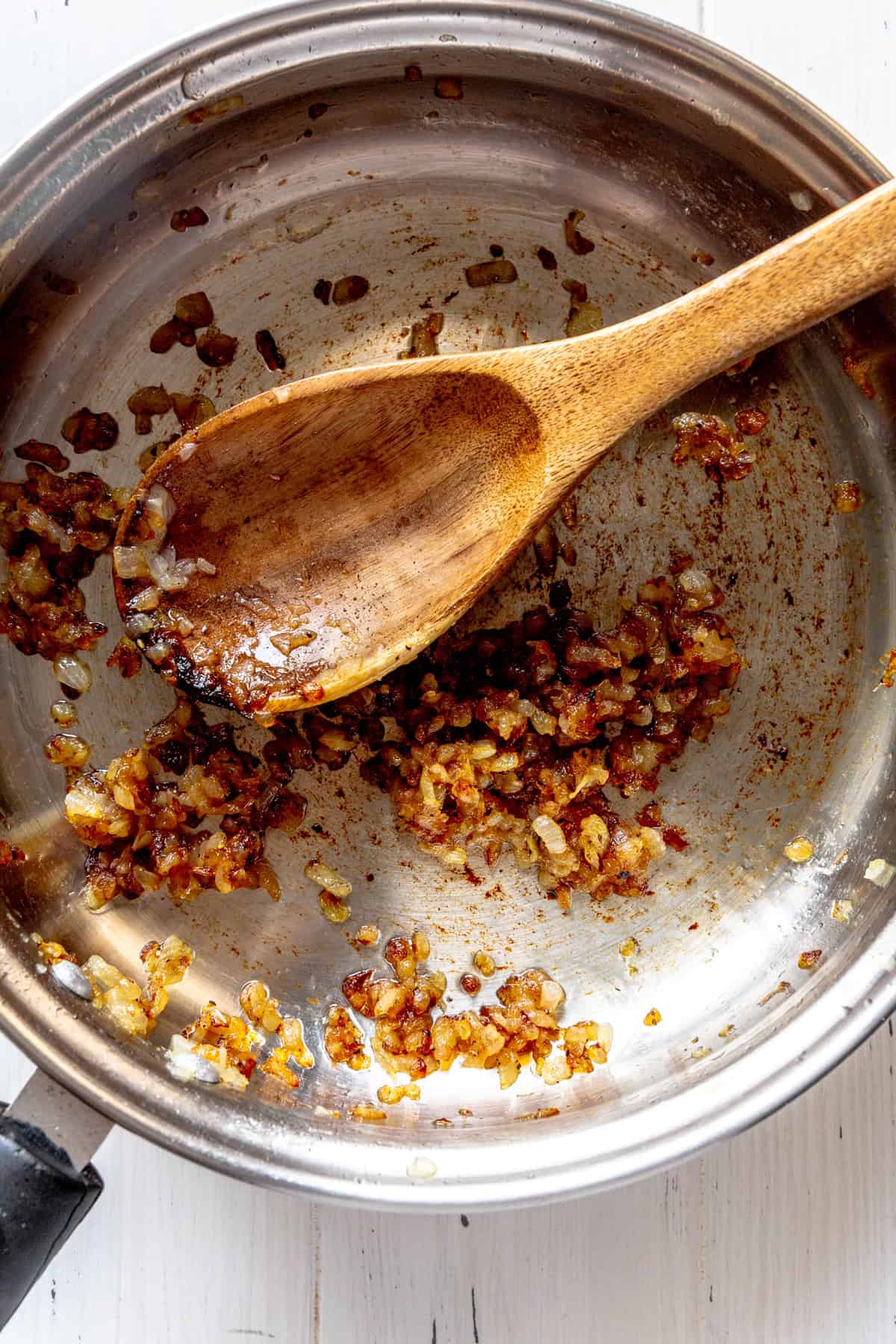 Caramelized onions in a skillet with a wooden spoon.