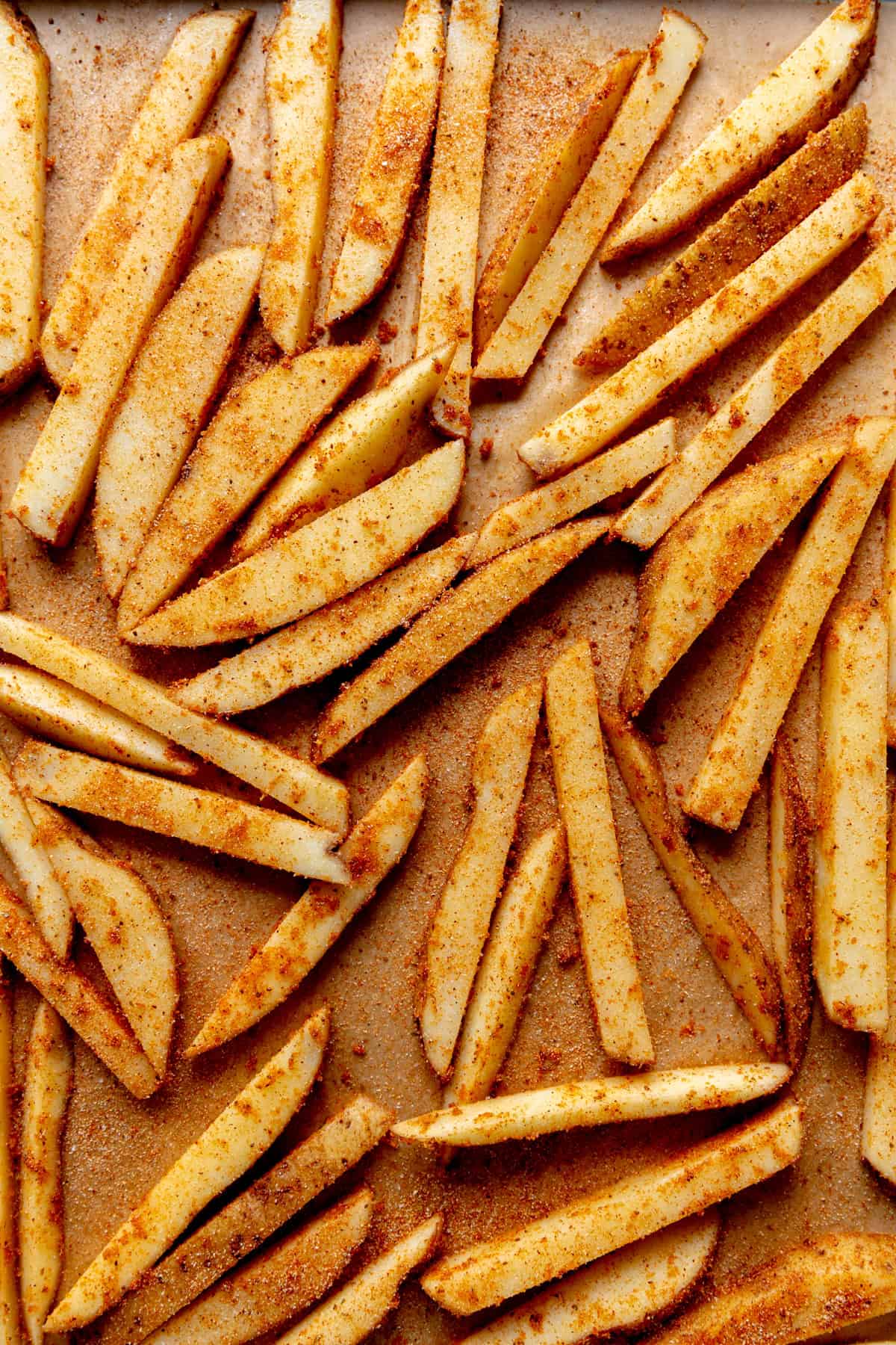 Potato wedges covered in seasoning on a baking sheet.