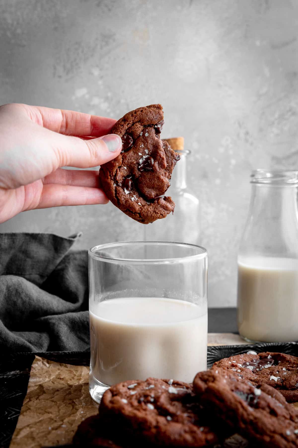Hand dunking a double chocolate cookie into a glass of milk.