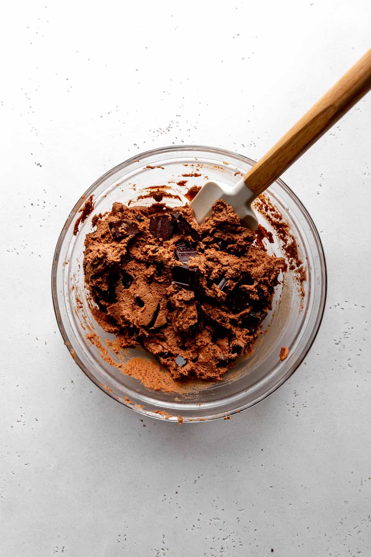 Chocolate cookie dough in a glass bowl with a rubber spatula.