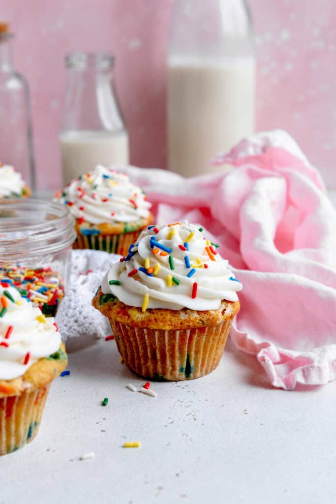 Funfetti cupcake, a jug of milk and a pink linen napkin.