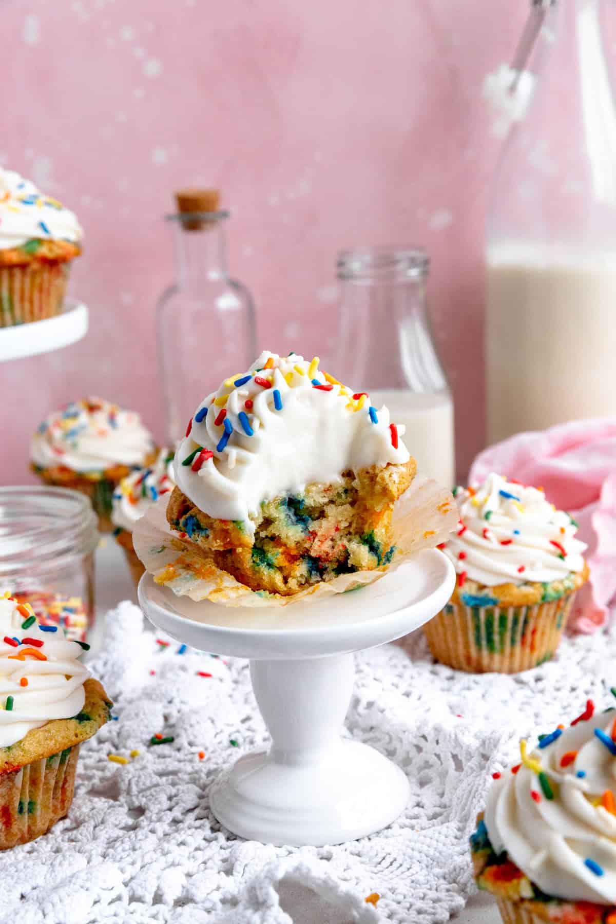 Funfetti cupcake with a bite taken out of it on a white pedestal.
