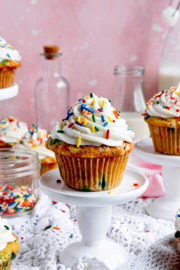 Vegan funfetti cupcakes on pedestals and a jug of milk.