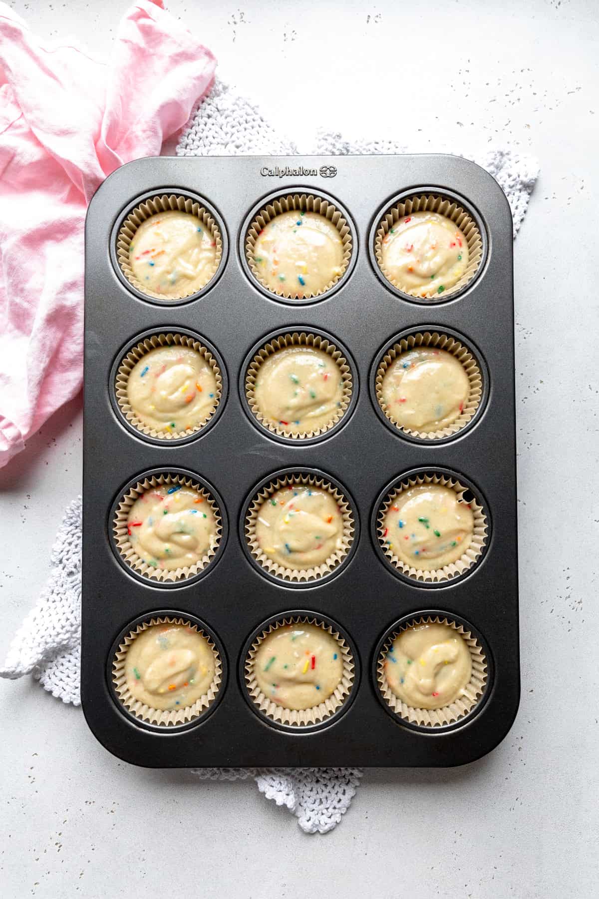 Unbaked cupcakes in a baking pan and a pink linen napkin.