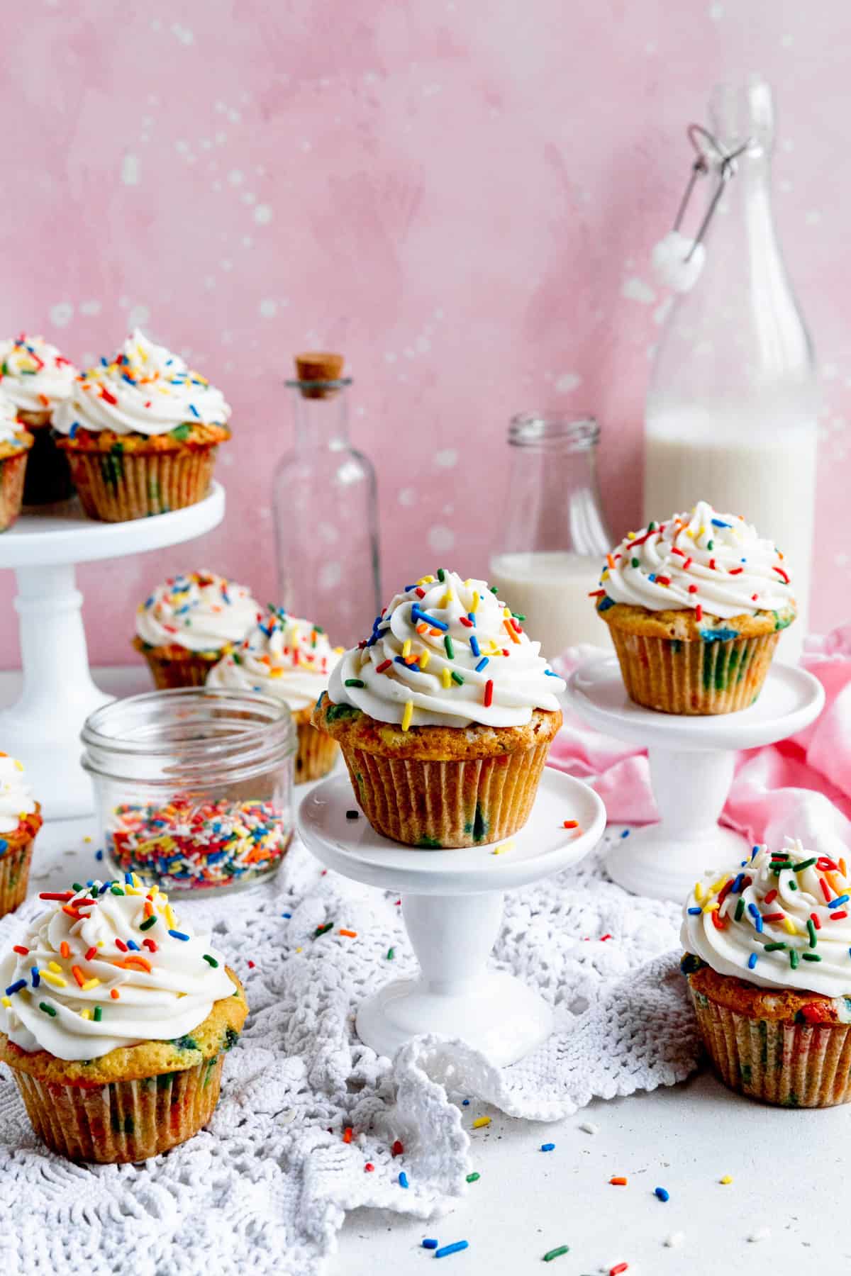 Funfetti cupcakes, a jar of sprinkles and two jugs of milk.