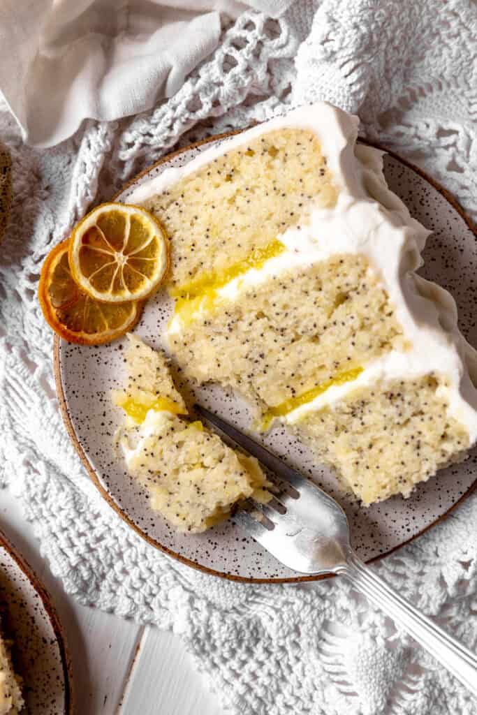 Fork cutting into a slice of lemon poppyseed layer cake.