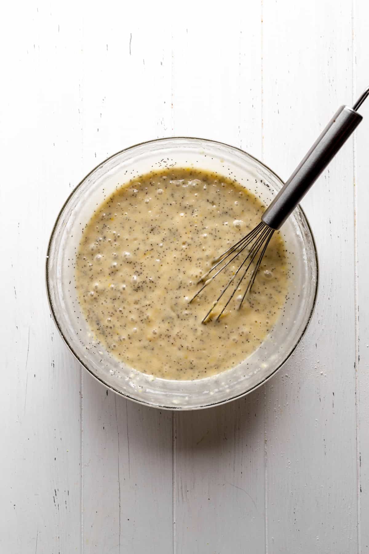 Lemon poppyseed cake batter in a glass bowl with a wire whisk.
