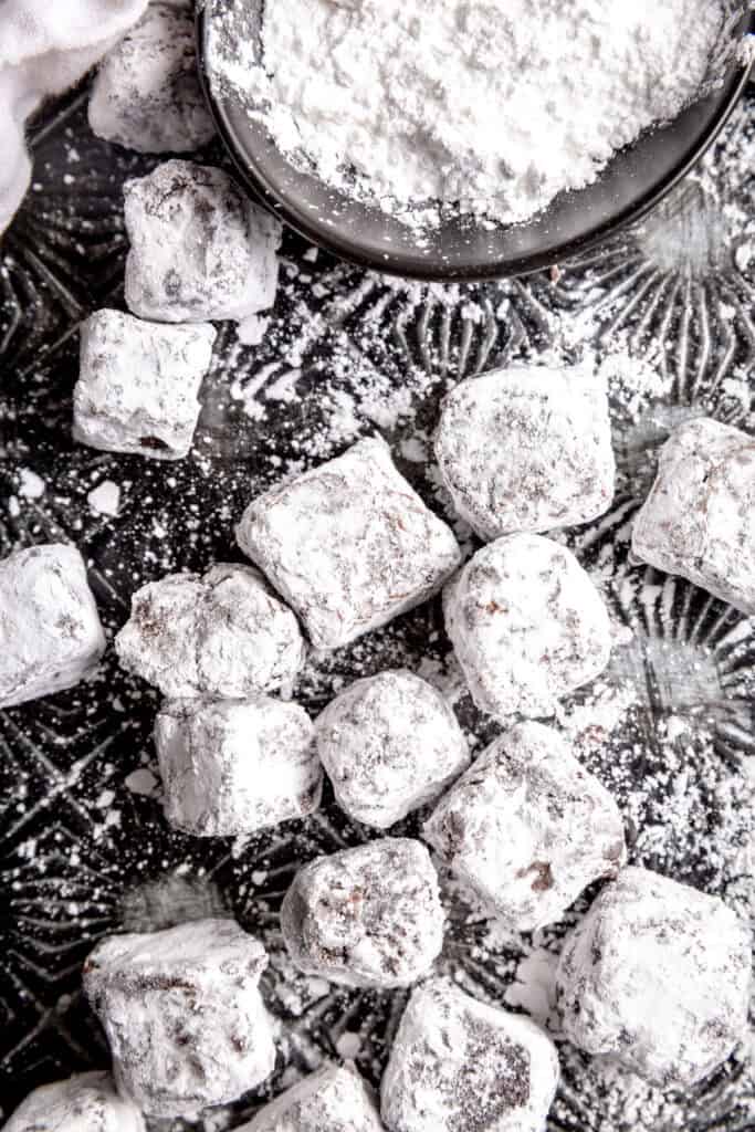 Brownie bites coated in powdered sugar and a cup of powdered sugar.