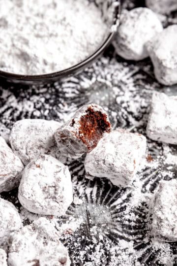 Brownie bite with a bite taken out of it with a cup of powdered sugar.