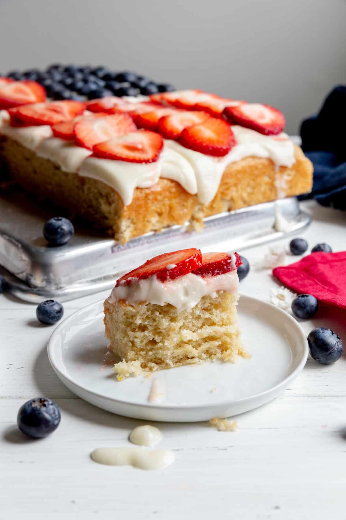 Half eaten piece of flag cake on a white plate surrounded by fresh blueberries.