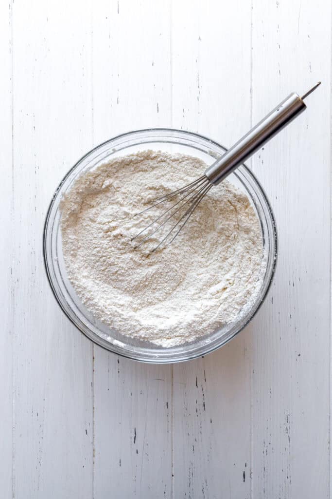 Glass bowl of flour and a whisk.