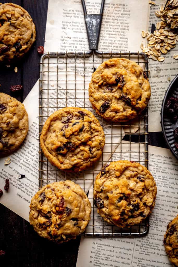 Oatmeal raisin cookies on a wire rack and a scoop of oats.