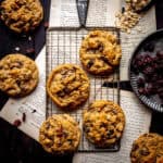 Oatmeal raisin cookies on a wire rack, a plate of raisins and a scoop of oats.