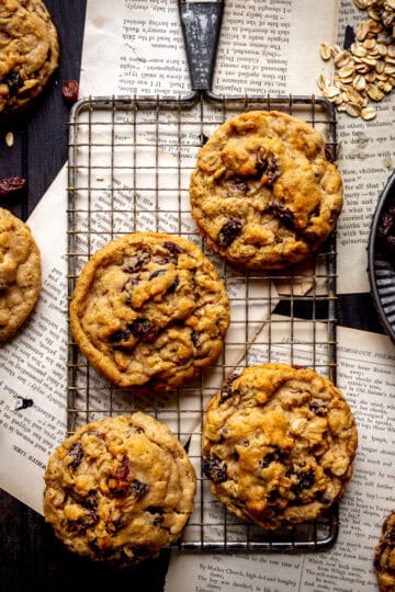 Oatmeal raisin cookies on a wire rack, a plate of raisins and a scoop of oats.