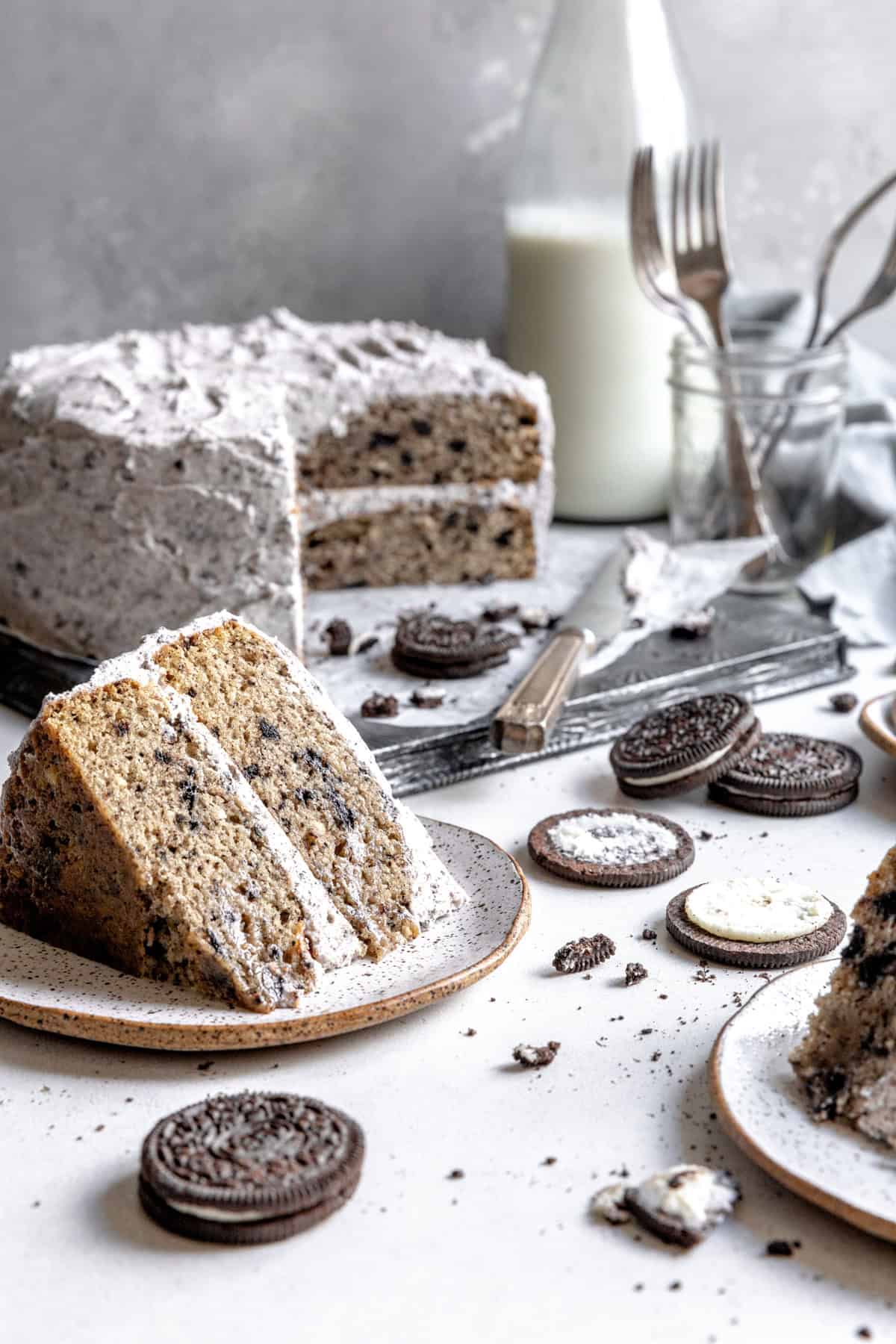 Pieces of oreo cake on plates, forks and a jug of milk.