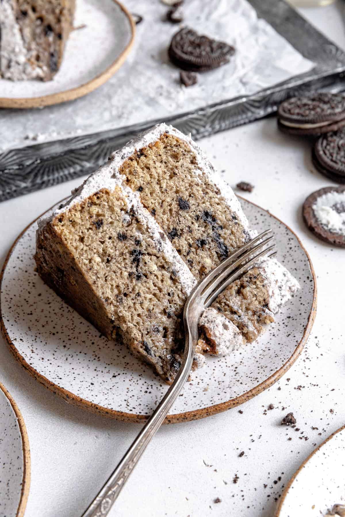 Fork cutting into a slice of oreo cake and a stack of oreos.