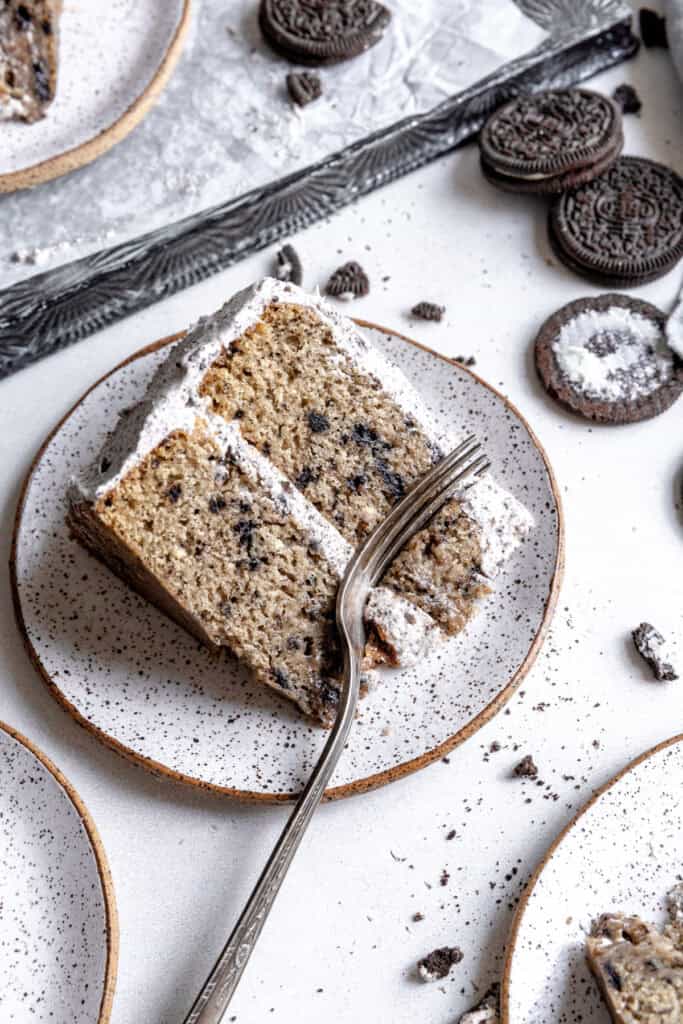 Fork cutting into a slice of oreo cake and a stack of oreos.
