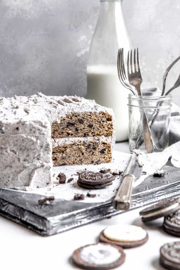 Oreo cake, a jar of forks, a jug of milk and scattered oreo cookies.