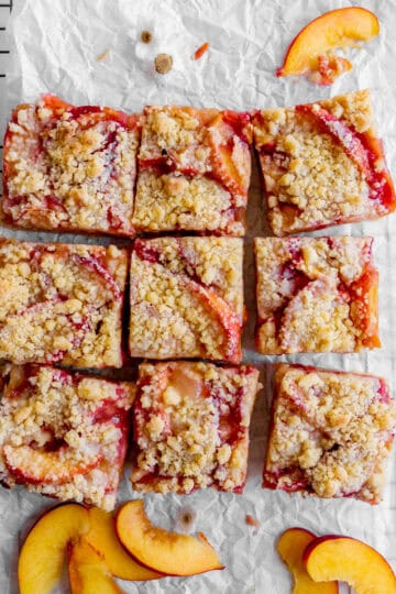 Peach Crumble Bars on a sheet of parchment paper with peach slices.