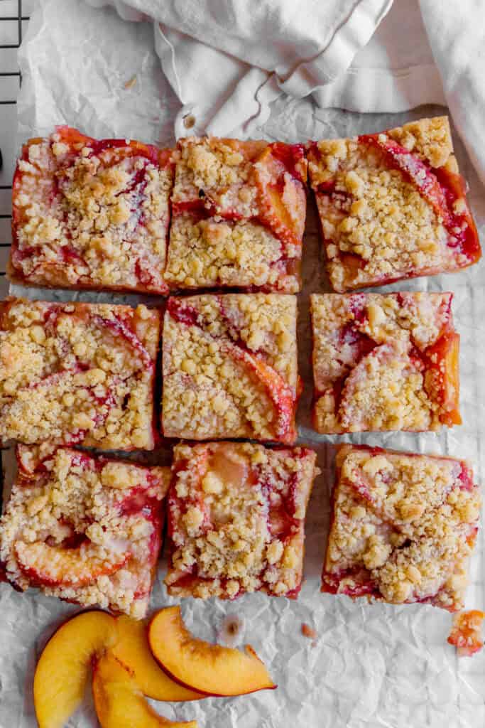 Peach crumble bars on white parchment paper and a linen napkin.