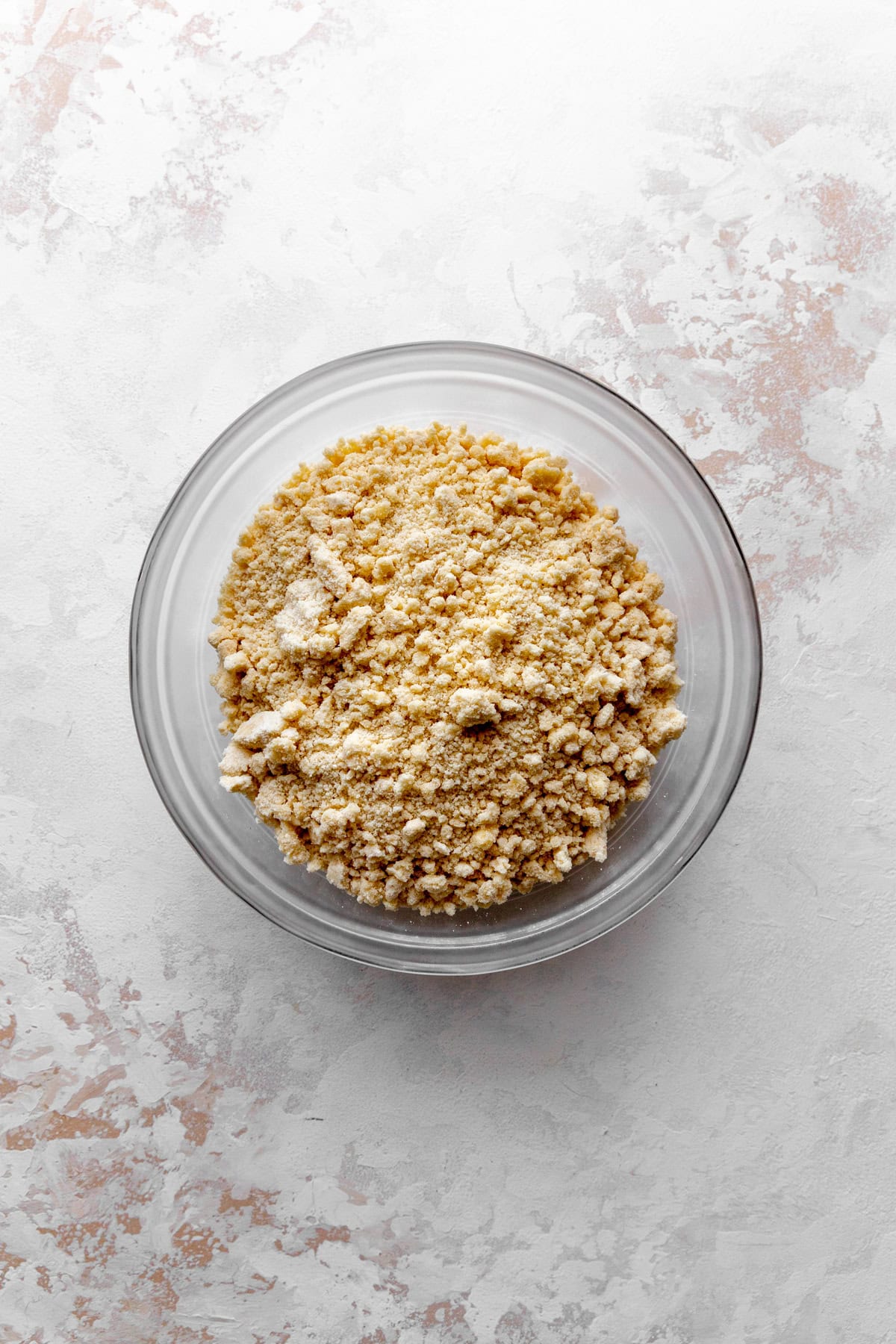 Glass bowl of butter crumbled into flour.