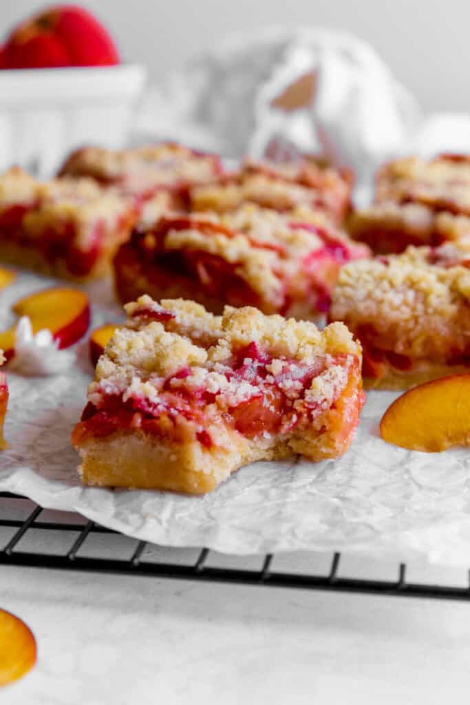 Peach crumble bar with a bite taken out of it and a basket of peaches.