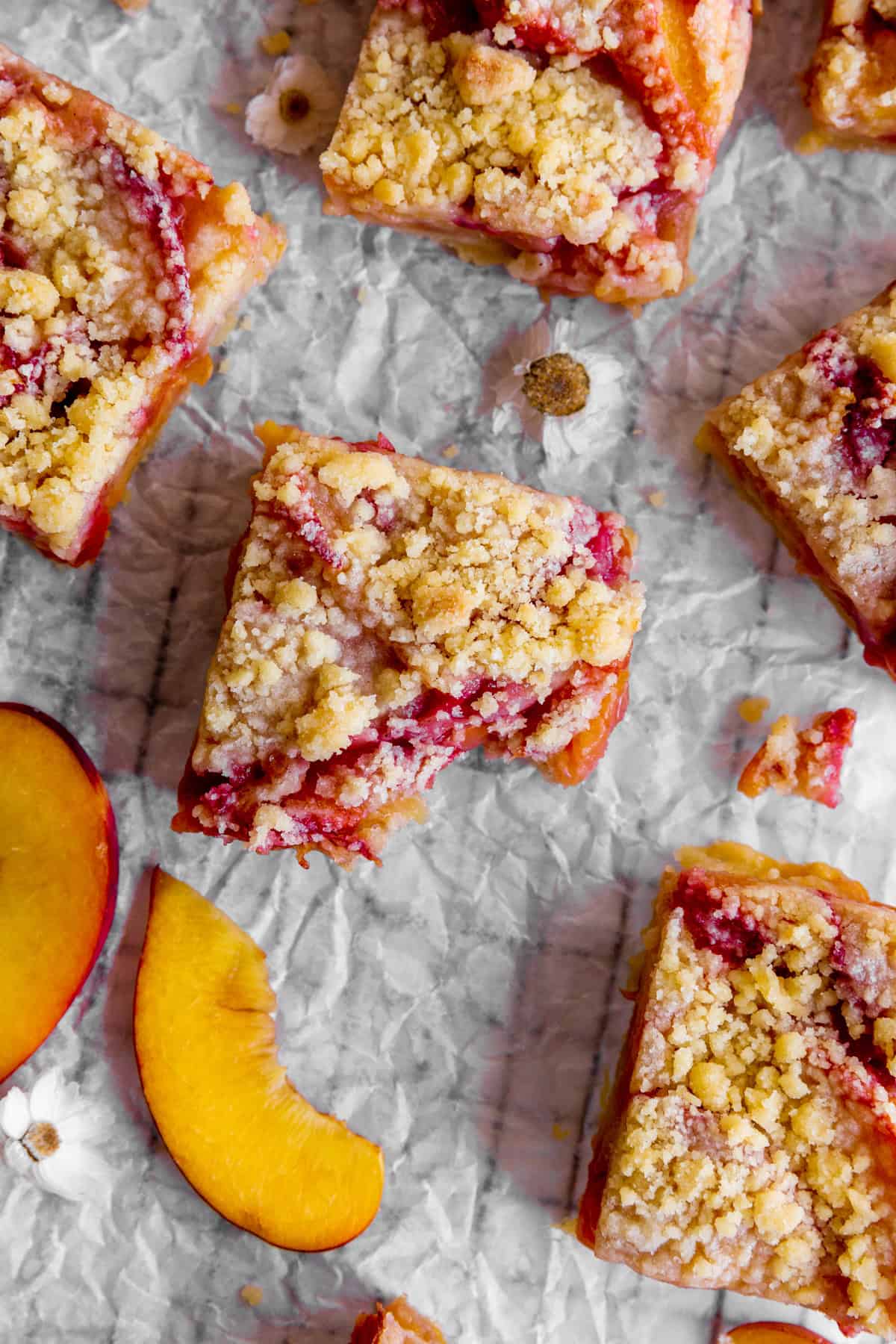 Peach crumble bar with a bite taken out of it and fresh peach slices.