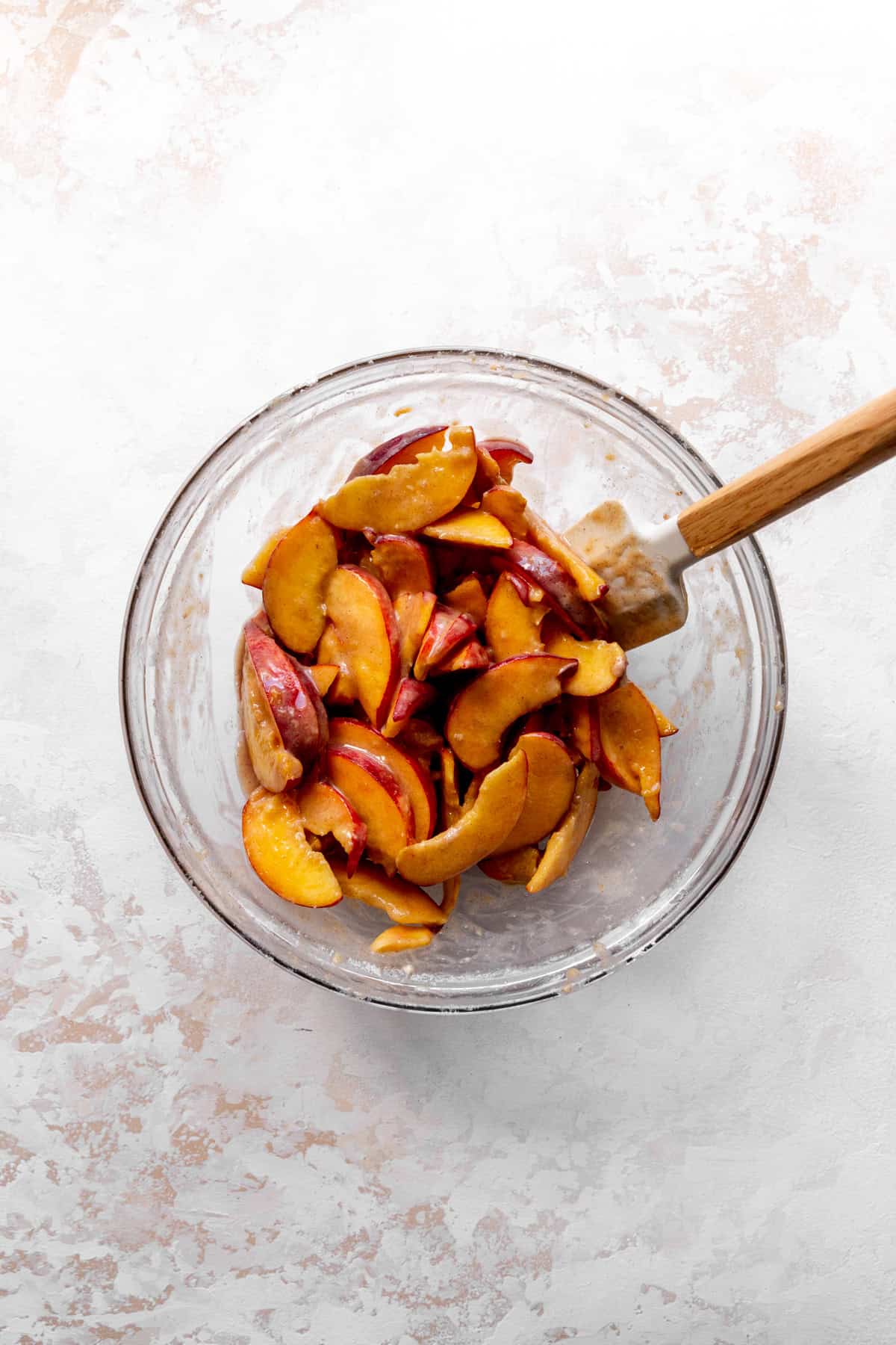 Glass bowl of peach slices with a rubber spatula.