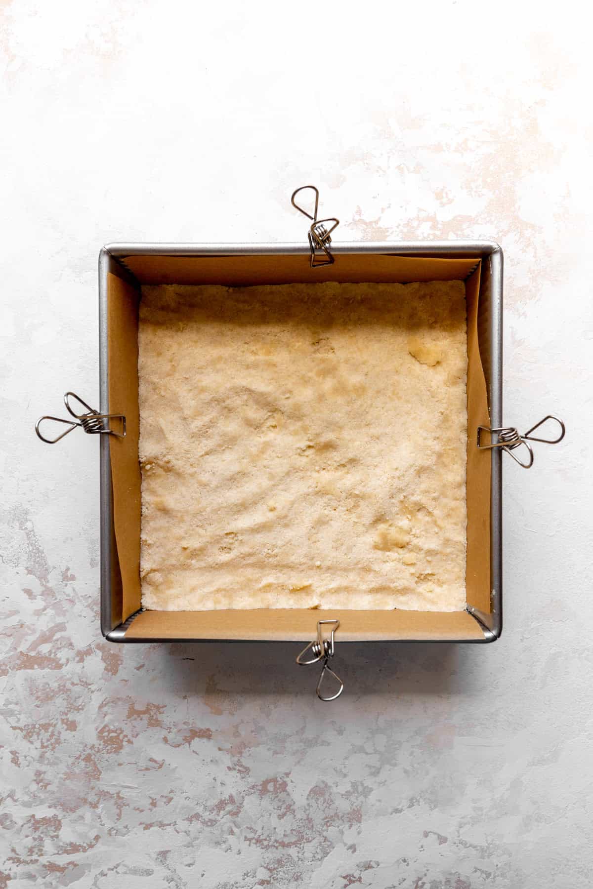 Crust pressed into a square pan lined with parchment paper.