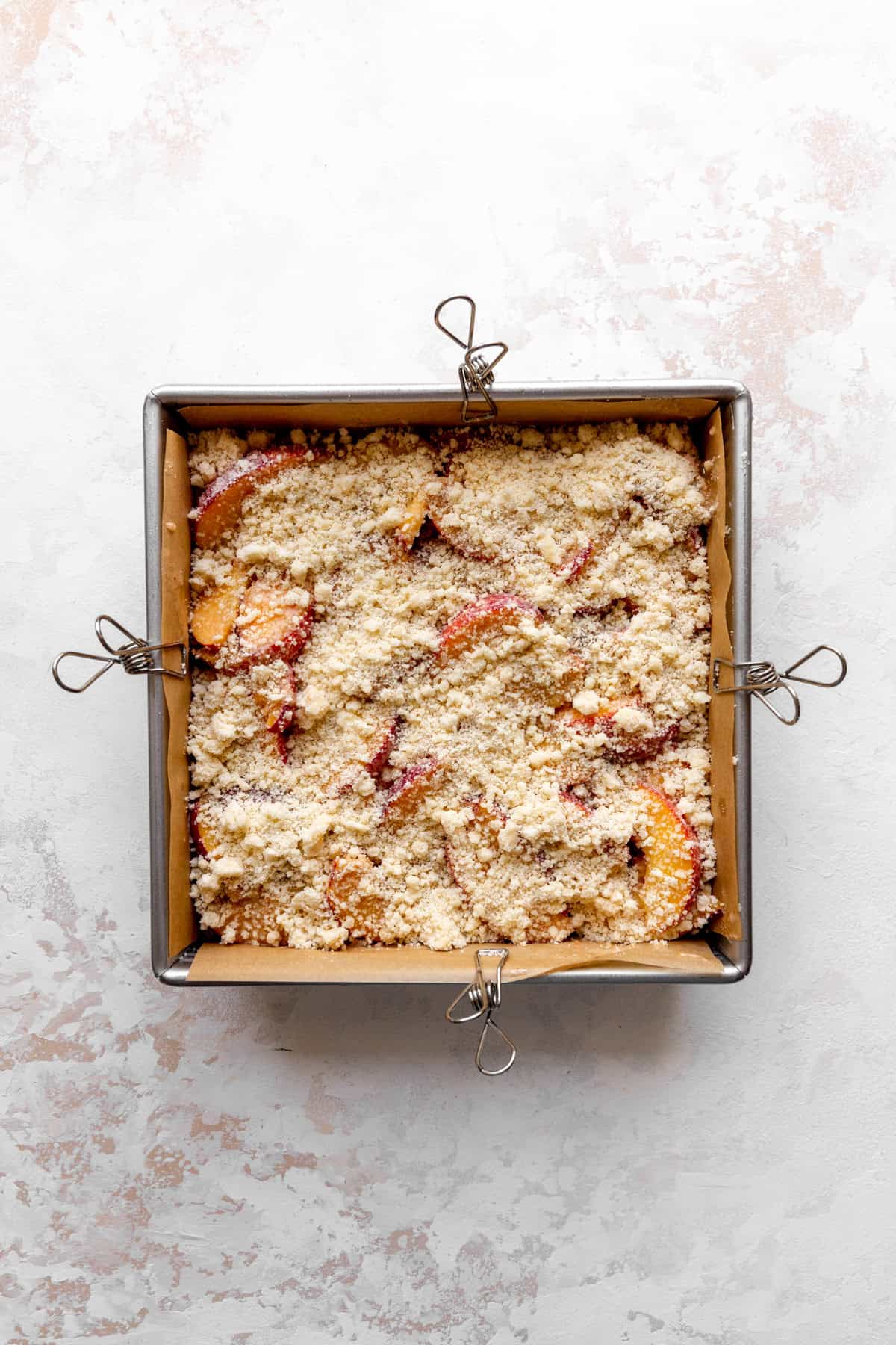 Unbaked peach crumble bars in a square pan.