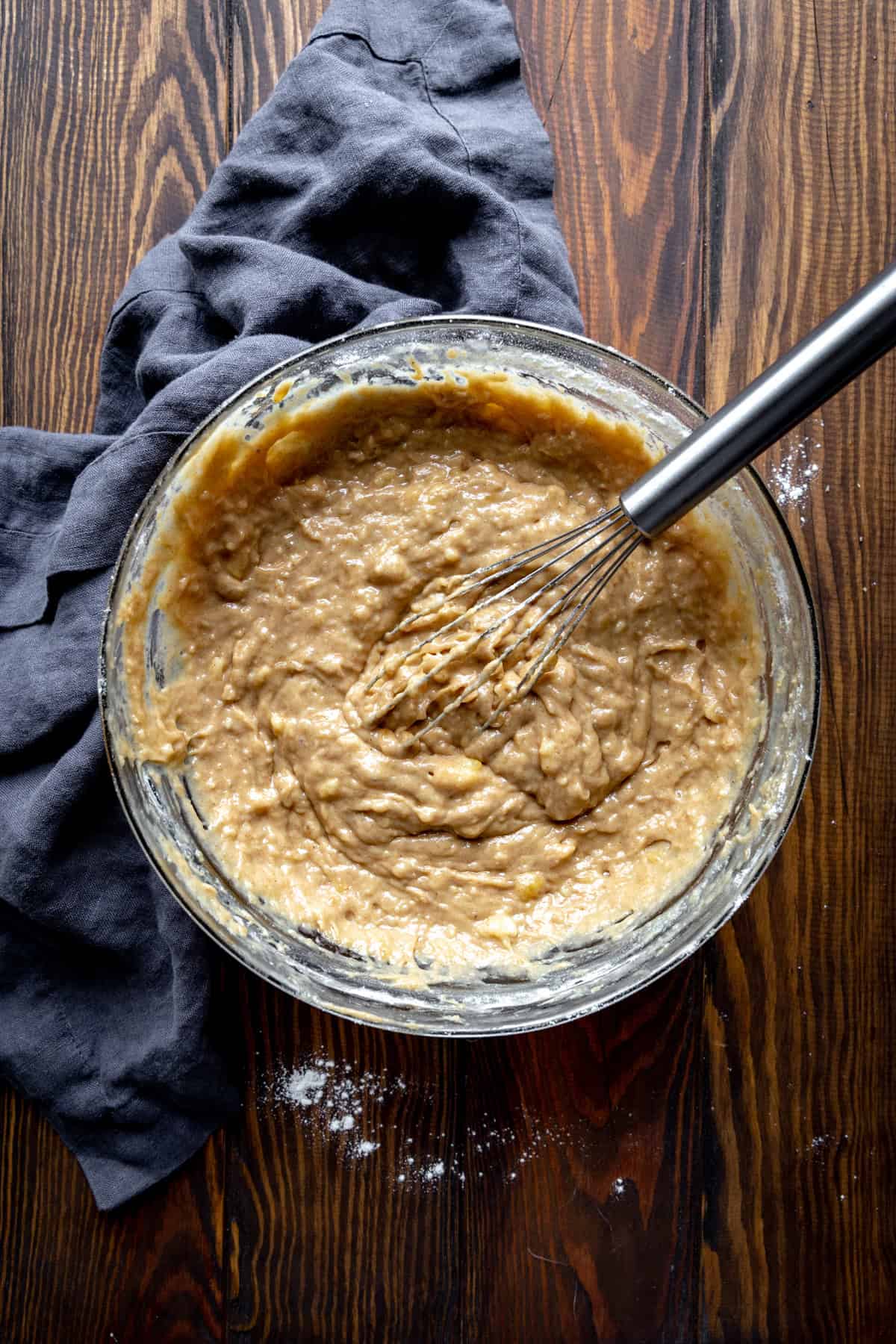 Peanut butter banana muffin batter in a glass bowl with a wire whisk.