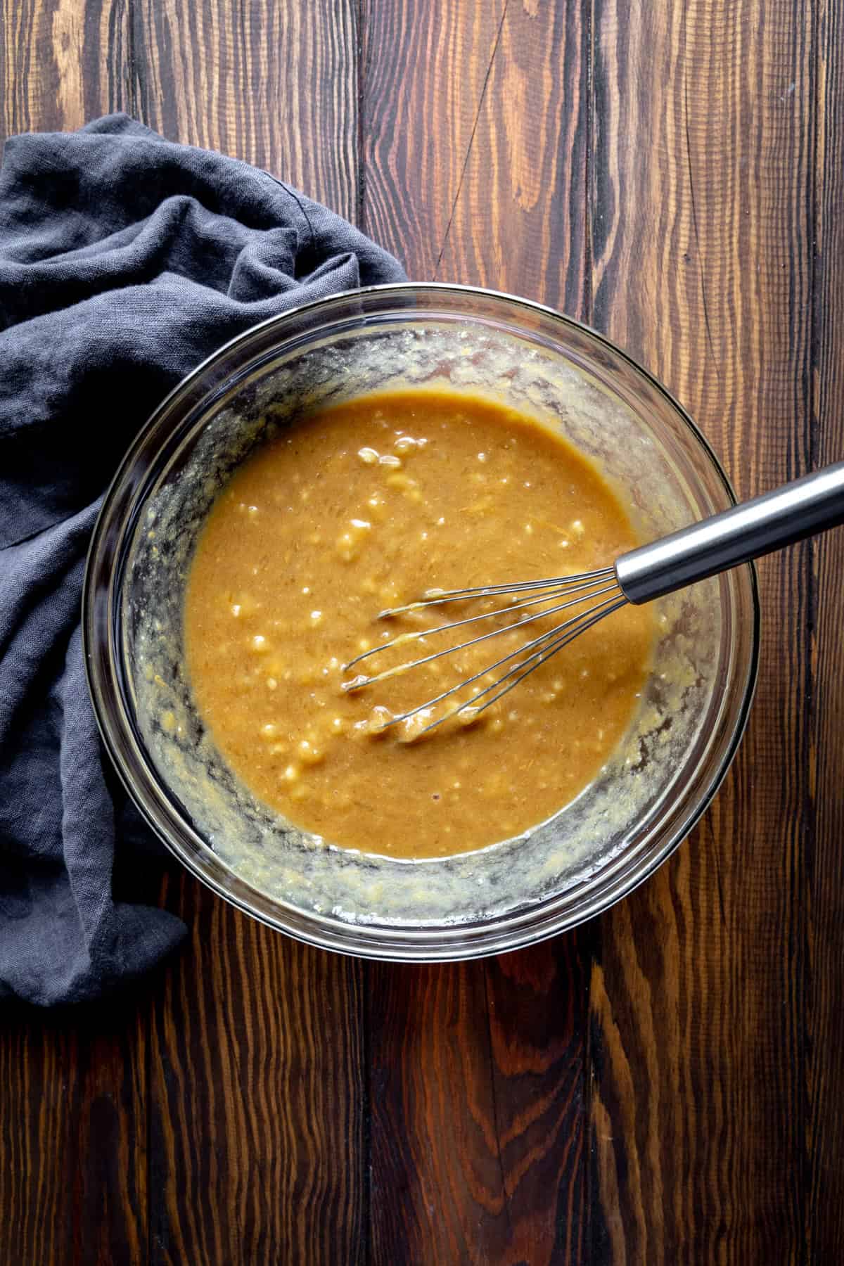 Mashed banana and peanut butter in a glass bowl with a wire whisk.