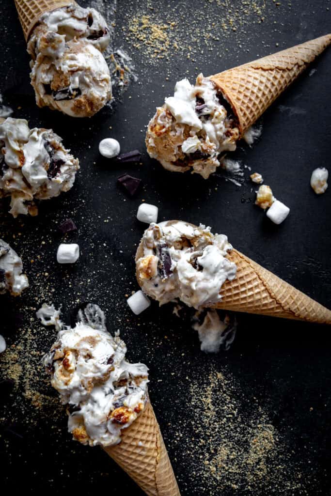 S'mores ice cream cones laying on a black surface with marshmallows and chocolate chunks.