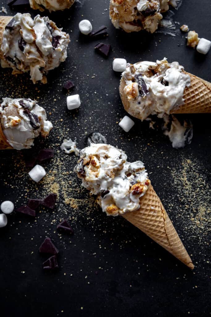 S'mores ice cream cones laying on a black surface with marshmallows and chocolate chunks.