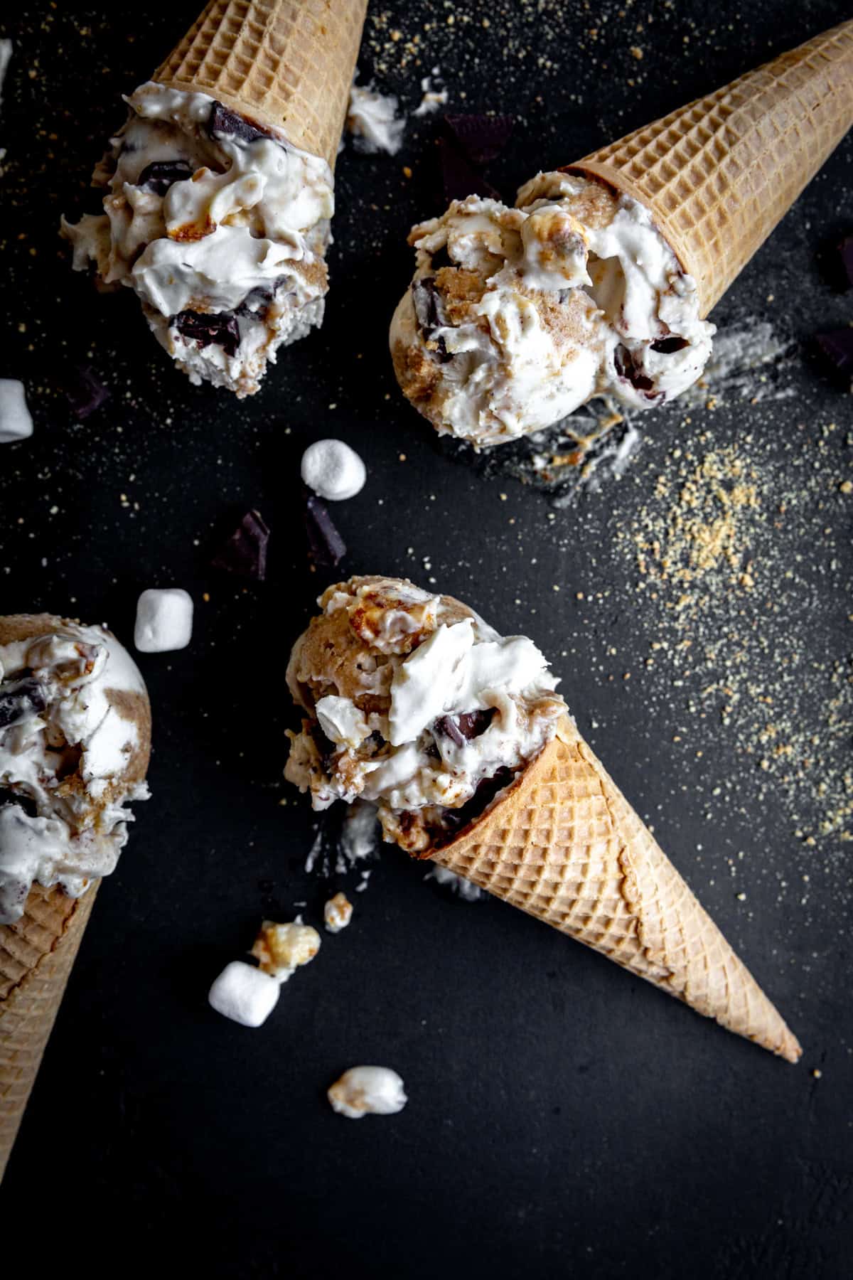S'mores ice cream in sugar cones on a black surface.