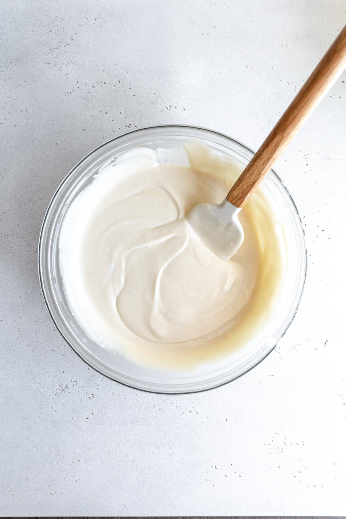 Vanilla ice cream base in a glass bowl with a rubber spatula.